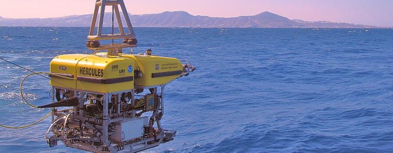 ROV Hercules being lowered into the water at sunset, with mountains in the background
