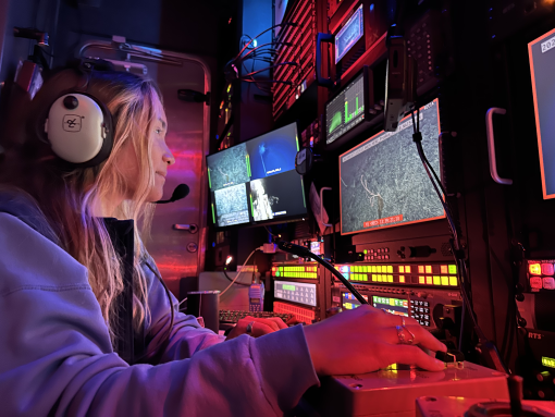 Video engineer Jaina sits in front of controllers in darkened control room